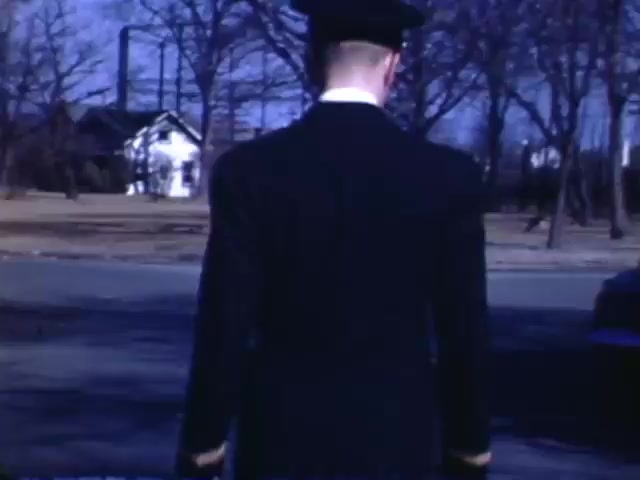 The still from 'Jack Reel 2' features a man in a military-style uniform, seen from behind, walking away from the camera. He appears to be in a residential area with leafless trees and a house in the background, indicative of winter or early spring. The vibrant colors typical of Kodachrome film from the early 1940s capture a nostalgic and historical atmosphere from the period between 1941 and 1943.