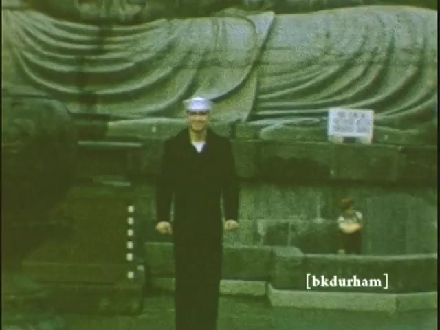 The 16mm still captures a moment from the 1959/1960 home movies featuring a man dressed in a sailor suit standing in front of the Great Buddha (Daibutsu) in Kamakura, Japan. The backdrop showcases the impressive statue, highlighting its serene expression and intricate details. A small child is seen sitting nearby, adding a sense of scale to the monumental figure. The scene evokes a nostalgic glimpse into mid-20th century travel and family memories in Japan.  Follow us on Twitter @FromFilm or like and subscribe here on YouTube.