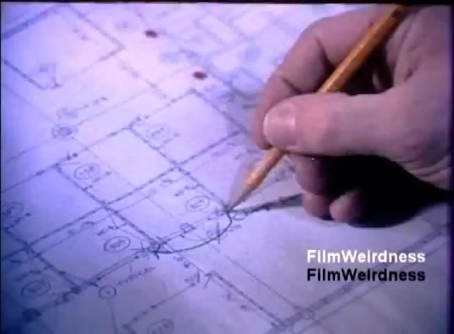 The still features a close-up of a hand holding a pencil, drawing on a blueprint. The blueprint has various architectural or technical symbols and diagrams, indicating a planned layout, likely related to the IBM System 36 technology. The scene suggests a focus on design and planning in a professional context.