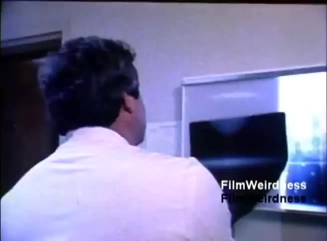 The still depicts a man in a white shirt, viewed from behind, looking at a projection or screen displaying an image, likely in a corporate or office setting. The environment appears plain, focused on the presentation. The context relates to IBM’s System 36, likely showcasing its functionalities or applications in a sales context.