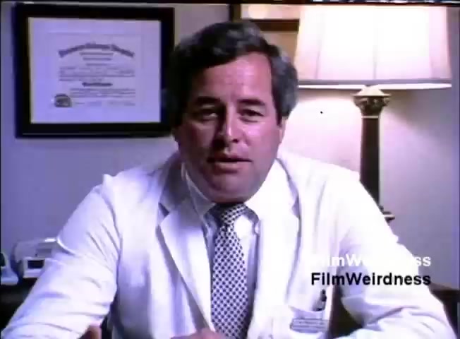 The still features a middle-aged man in a white lab coat, seated at a desk. He appears to be speaking directly to the camera. Behind him, there is a framed diploma or certificate on the wall, and a lamp is positioned beside him, creating a warm lighting effect. The context of the image relates to the IBM System 36 sales film from 1984, likely featuring testimonials or endorsements for the product.