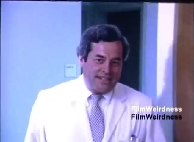 The still features a man in a white suit and tie, looking directly at the camera with a slight smile. The setting appears to be an office or clinical environment, characterized by bright lighting and plain walls. The tone suggests a professional or business context, likely related to the promotion of the IBM System 36. The overall atmosphere is friendly and welcoming.