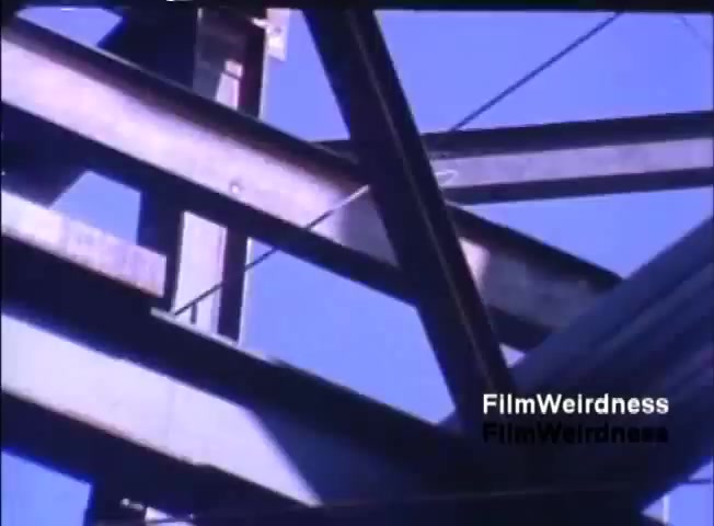 The still shows a close-up view of metal beams and structures, likely part of a larger framework or building. The image captures the geometric lines and angles created by the steel architecture against a bright blue sky, emphasizing industrial design. The lighting suggests a sunny day, highlighting the metallic surfaces. This imagery aligns with the promotional context of the IBM System 36 sales film, possibly illustrating the robust infrastructure associated with modern technology.