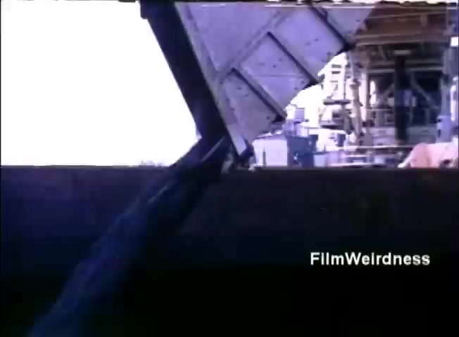 The still from the IBM System 36 sales film shows a semi-automated industrial setting, likely involving heavy machinery or a loading mechanism. An angled view captures a metal structure, possibly part of equipment or a conveyor, with a light background suggesting an outdoor or brightly lit environment. Overall, it conveys the technological context and operational workflow relevant to IBM's marketing of their computing systems in the 1980s.