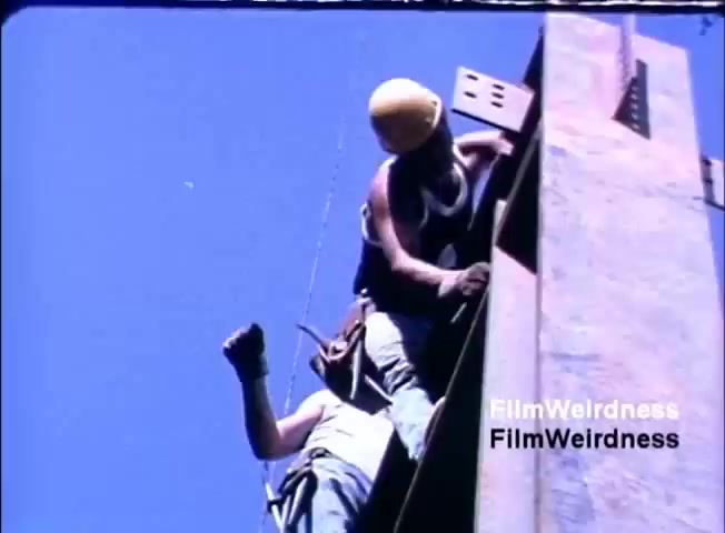 The still features two construction workers on a steel beam, showcasing a dynamic and upward-focused perspective. One worker wears a yellow hard hat and appears to be assisting the other, who is climbing. The sky above is clear blue, suggesting a sunny day. This imagery likely symbolizes progress and teamwork, aligning with the themes of the IBM System 36 sales film, which may emphasize innovation and collaboration in business environments.