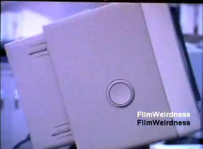 The still features a close-up of an IBM System 36 unit from the 1984 sales film. The device is presented in a grayish casing with a prominent circular button on its front. The background appears blurred, suggesting a focus on the hardware, indicative of the marketing emphasis on the system's design and functionality.