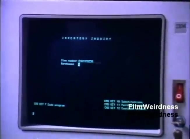 The still features an IBM display screen showcasing a program interface labeled 'INVENTORY INQUIRY.' The screen displays a prompt for 'Item number' and 'Barcodes,' indicating it's part of a system designed for inventory management. The surrounding monitor appears classic for the 1980s, marked by IBM branding, with visible control buttons on the side. The aesthetic reflects the early computer technology used in business settings during that era.