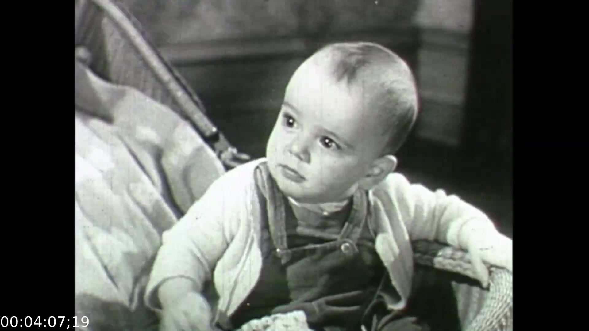The still from 'Feelings of Depression' (1950) features a baby with a contemplative expression, seated in a wicker chair. The simplicity of the child's clothing and the background hints at the mid-20th century setting. This image symbolizes the innocence and vulnerability associated with childhood, contrasting with the film's focus on adult struggles with depression, particularly through the character of John Murray. The juxtaposition highlights the emotional impacts of mental health across different life stages.