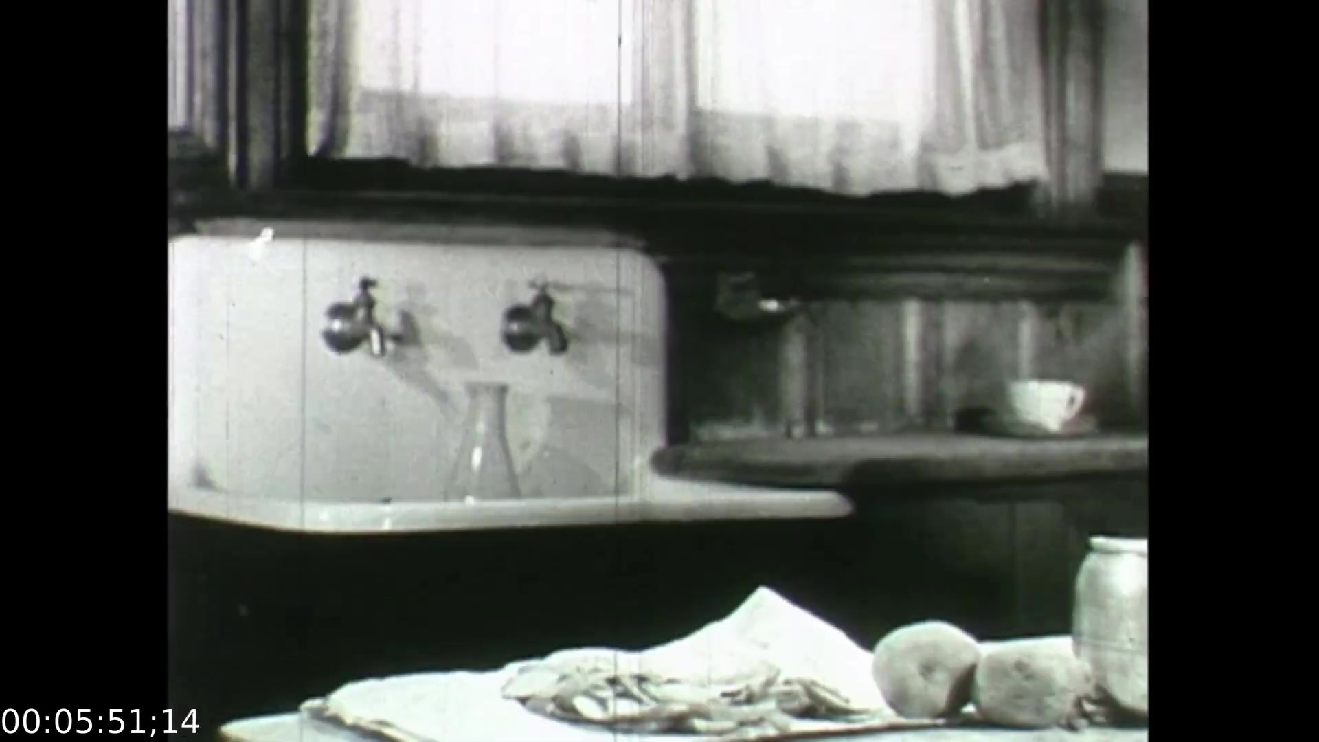 The still from 'Feelings of Depression' captures a domestic kitchen setting, emphasizing simplicity and functionality. A white countertop hosts a variety of items including a jar, a glass container, and fruit, suggesting a sense of everyday life. The muted color palette and vintage aesthetic reflect the era of the film, highlighting the emotional isolation of the protagonist, John Murray. This setting serves as a visual metaphor for the struggle with mental health portrayed in the film, juxtaposing ordinary domesticity with underlying emotional turmoil.