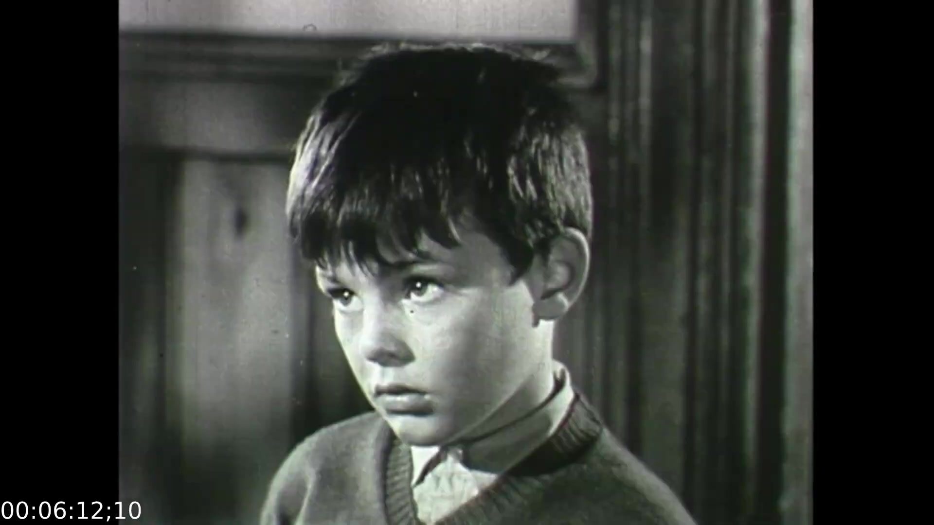 The still from 'Feelings of Depression' presents a young boy with a serious expression, indicating a sense of concern or reflection. His gaze suggests he is involved in a significant moment, possibly related to the themes of the film. The black-and-white format enhances the emotional gravity of the scene, typical of the era's educational dramatizations. This film aims to shed light on mental health, particularly the impacts of depression on individuals and their families.