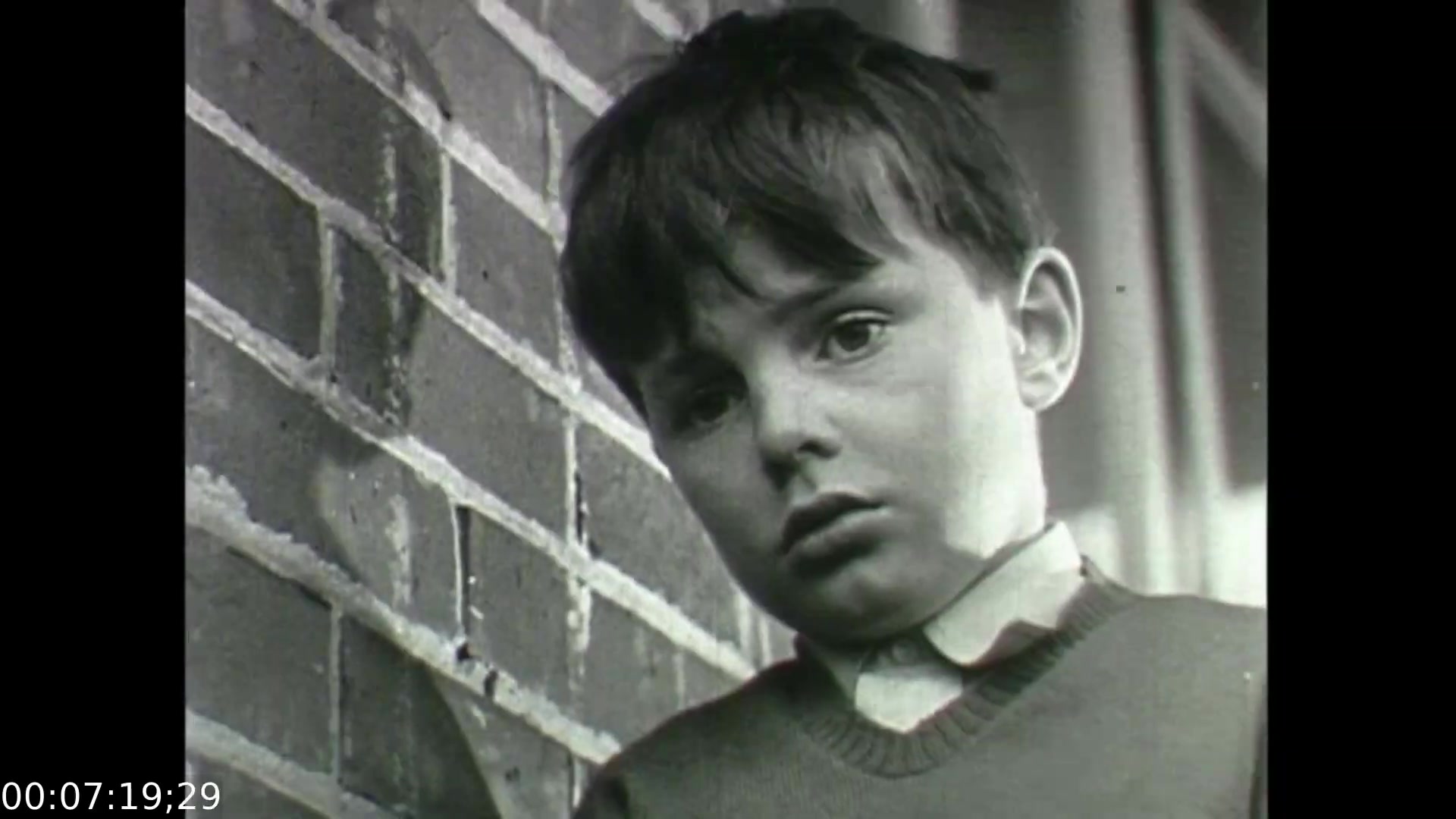 The still from 'Feelings of Depression' depicts a young boy with a somber expression, standing against a brick wall. His downcast gaze and seemingly troubled demeanor reflect themes of emotional distress, aligning with the film's exploration of depression and mental health. This image likely represents the impact of early emotional experiences on individuals, setting the stage for understanding the complexities of adult despondency, as seen in the character of John Murray. The stark black-and-white style emphasizes the gravity of the subject matter.