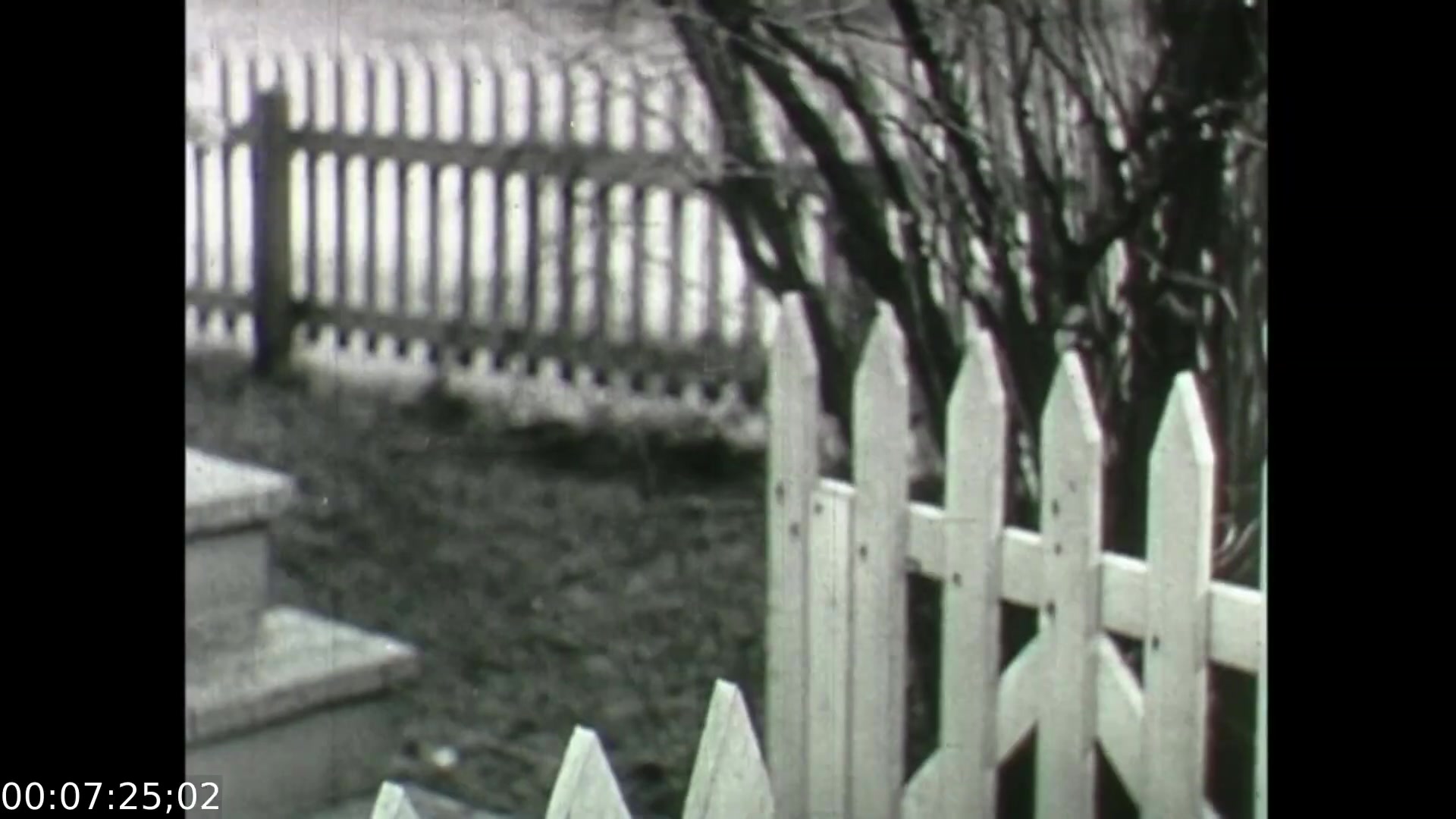 The 16mm still from 'Feelings of Depression' (1950) shows a bleak outdoor scene featuring a white picket fence and barren trees, indicative of an early spring or late winter setting. The fence, symbolizing boundaries, contrasts with the desolate surroundings, reflecting the isolation and emotional struggles of the protagonist, John Murray. The overall composition evokes a sense of despondency, aligning with the film's exploration of mental health issues in a historical context.