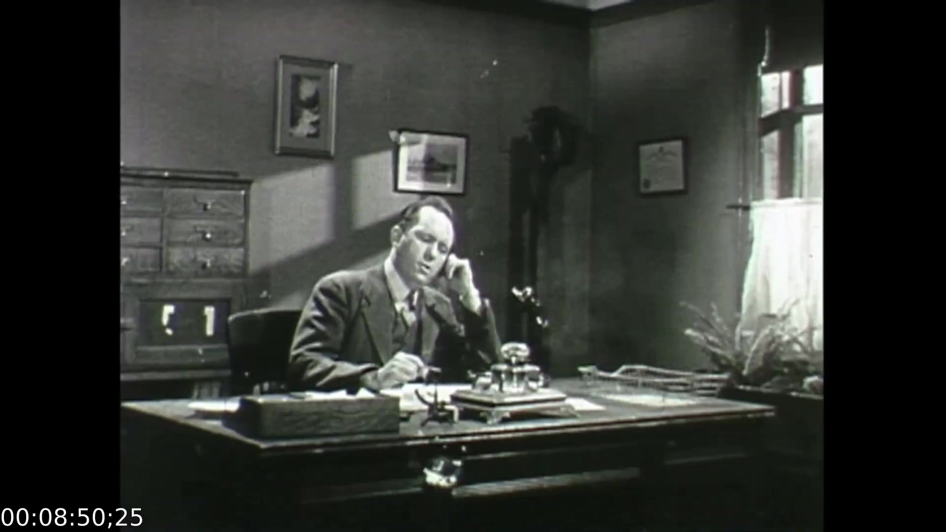 The still from 'Feelings of Depression' (1950) depicts a man, likely John Murray, sitting at his desk in an office setting. He appears contemplative, holding a pen and looking off into the distance, suggesting a moment of introspection or concern. The office is sparsely decorated, with a combination of furniture and artworks that reflect mid-20th-century design. This scene captures the film's focus on the emotional struggles faced by the character, highlighting the themes of mental health and its impact on an individual's life and work.