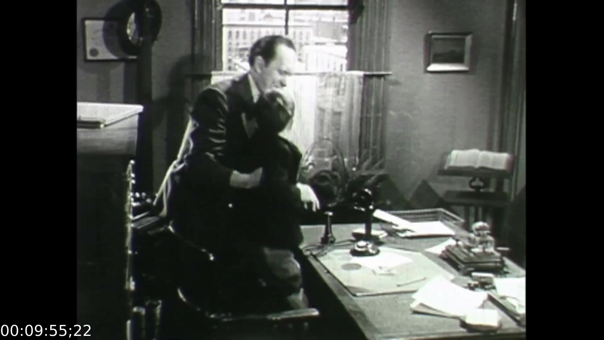 In this still from 'Feelings of Depression' (1950), a man is shown embracing another individual in an office setting, conveying a moment of emotional support. The background features a window with a view of a cityscape, alongside a cluttered desk filled with papers and office supplies, reflecting the stress of the character's life. This scene illustrates themes of struggle and connection amid the challenges of mental health, focusing on the character of John Murray, a businessman grappling with depression.