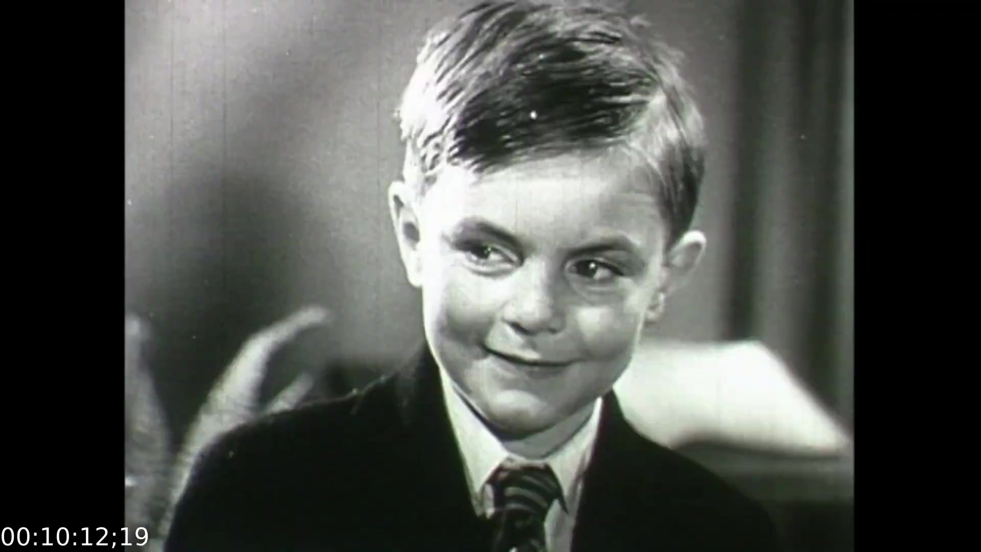 The still features a young boy with a subtle smile, dressed in a suit with a tie. His expression suggests a mix of curiosity and innocence. The context of the film 'Feelings of Depression' emphasizes the emotional struggles faced by individuals, reflecting the impact of mental health issues during the era. This image captures a moment that contrasts the film's serious themes with a youthful perspective, potentially illustrating early familial or social dynamics that may influence mental well-being.