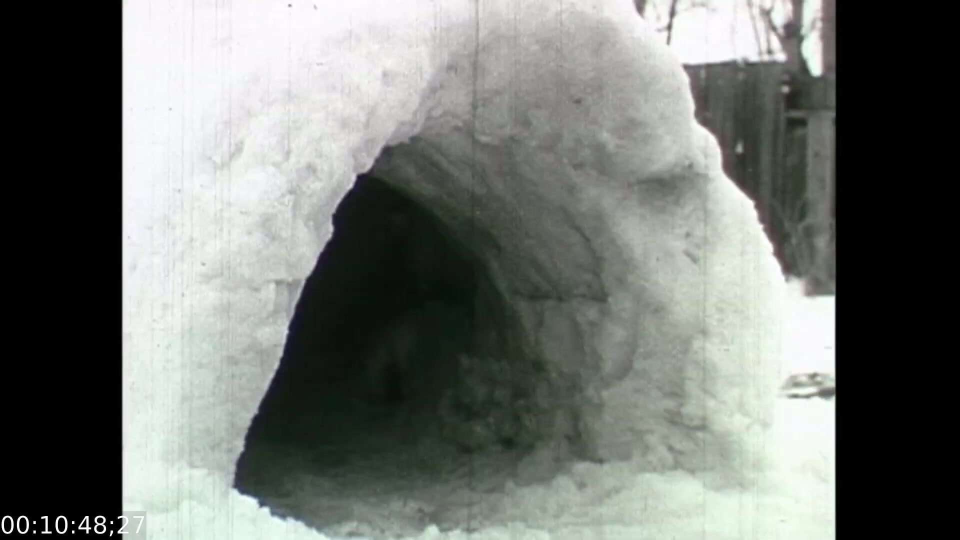 The still from 'Feelings of Depression' features a snow cave or tunnel, emphasizing a theme of isolation and introspection. The snowy environment symbolizes desolation, reflecting the emotional struggles of the protagonist, John Murray. This scene likely serves to illustrate the heaviness of depression, contrasting with the expectations of a warm, inviting space. The use of monochrome further enhances the somber tone of the film, capturing the bleakness associated with mental health challenges in the 1950s.