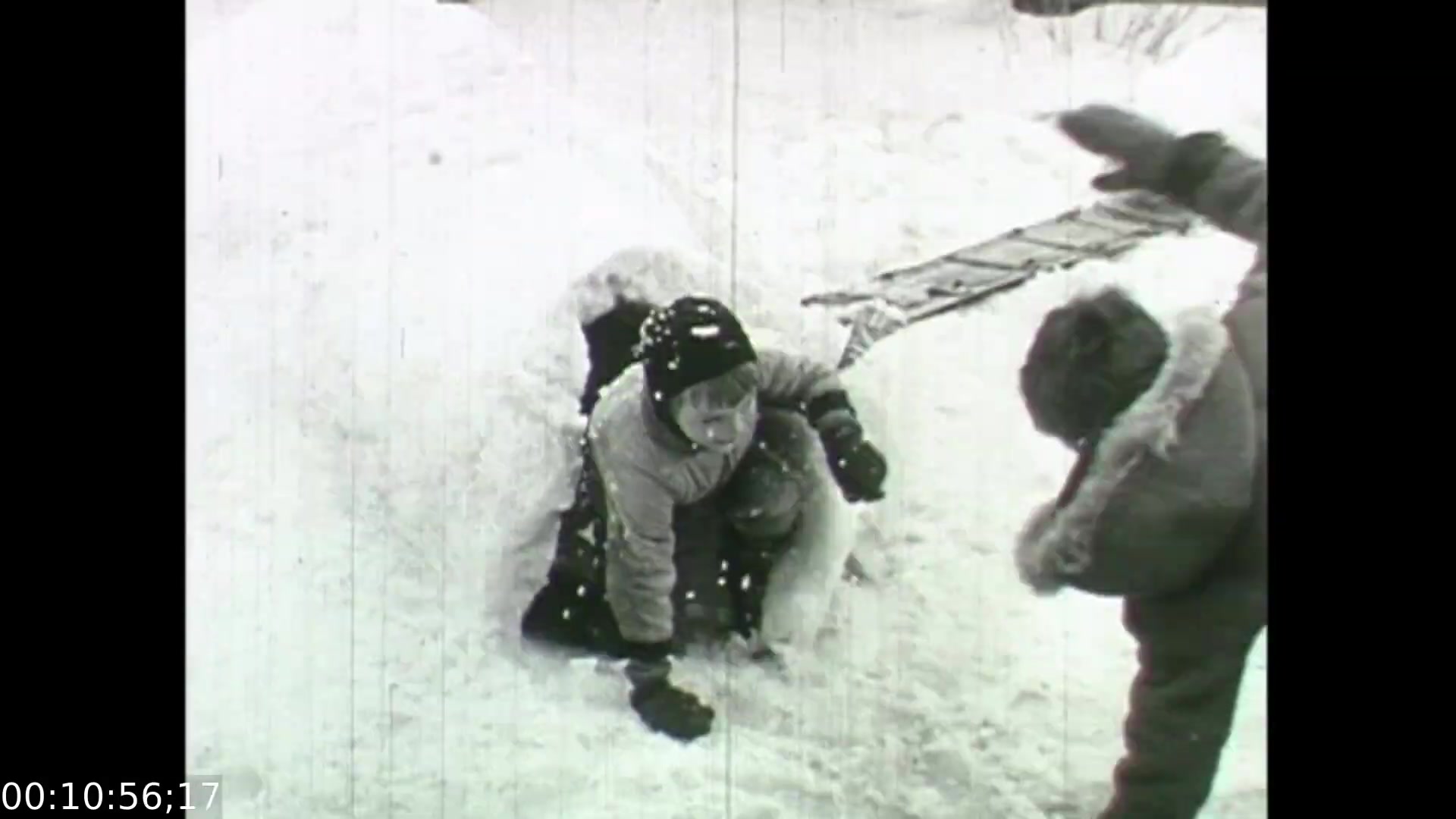 The still from 'Feelings of Depression' depicts a snowy outdoor scene where a child is emerging from a snowbank, indicating playful engagement. Another figure, presumably an adult, reaches out toward the child, possibly assisting or encouraging them. This moment captures the contrast between childhood innocence and the underlying themes of emotional struggle explored in the film, which seeks to address the complexities of mental health through relatable narratives. The visual aesthetic reflects the era's filmmaking style, highlighting both the starkness of winter and the warmth of human interaction.