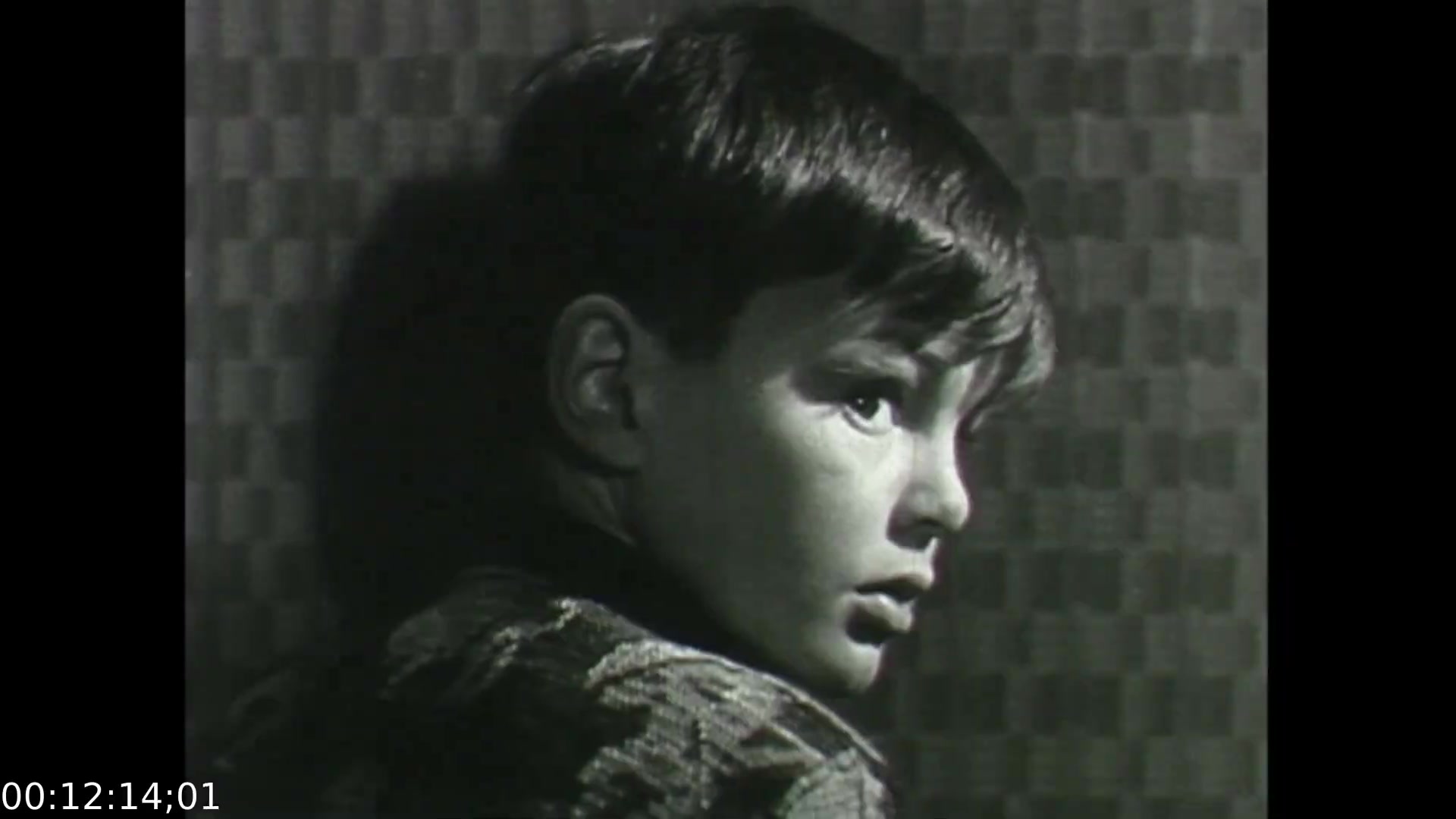 The still from 'Feelings of Depression' (1950) features a young boy in profile, conveying a sense of introspection or sadness. The use of chiaroscuro lighting highlights his facial features, emphasizing the emotional weight of his expression. The textured background adds depth, creating a stark contrast with the boy's somber demeanor. This visual representation aligns with the film's exploration of mental health, illustrating the impact of emotional struggles from an early age.