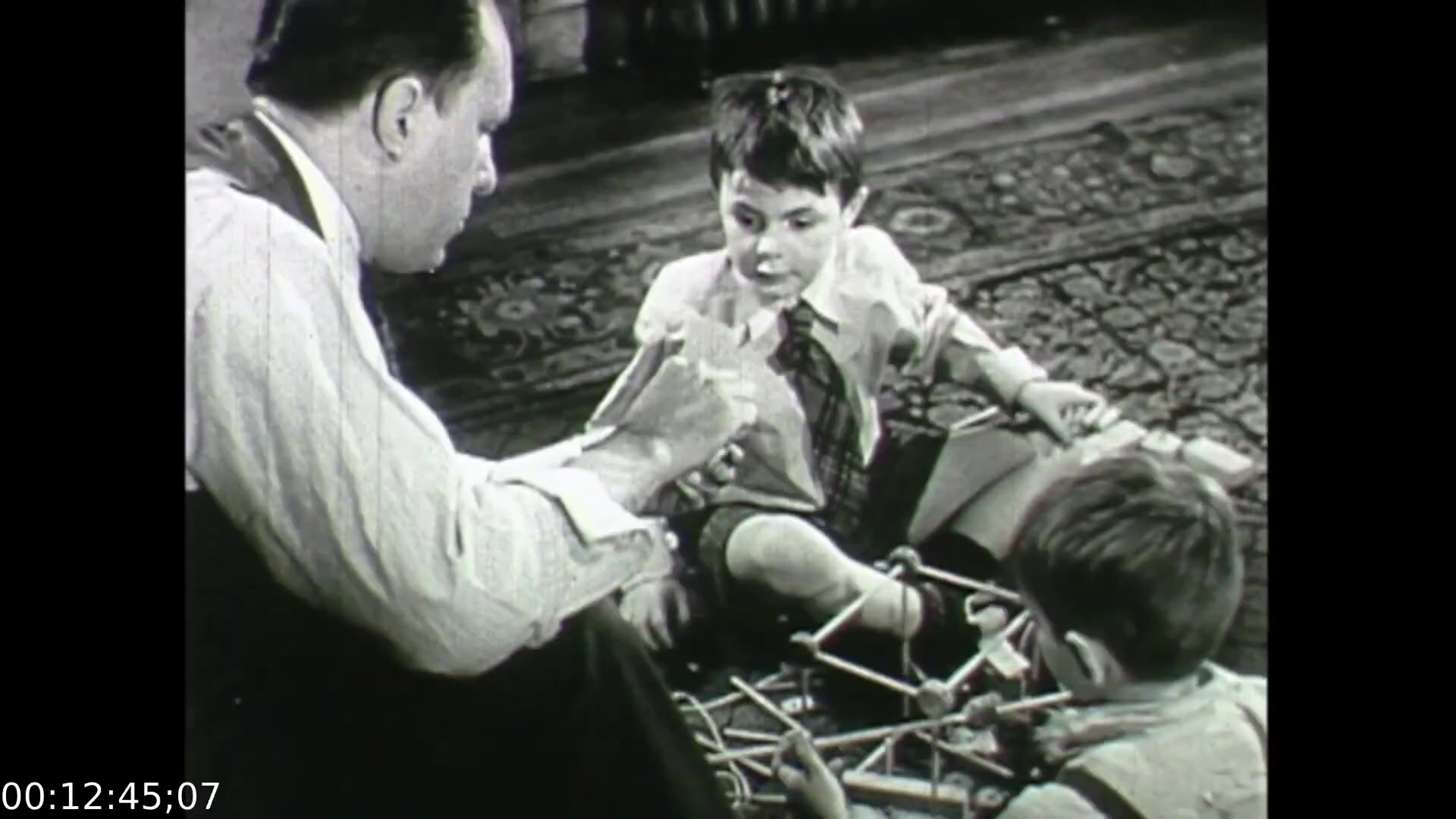 The still from 'Feelings of Depression' (1950) shows a pivotal moment where an adult man engages with two young boys, fostering a moment of connection through play. The scene underscores themes of familial interaction and the importance of emotional support in childhood development. This educational film highlights the impact of depression not only on individuals but also on their relationships with loved ones, illustrating a holistic approach to mental health awareness in post-war Canada.