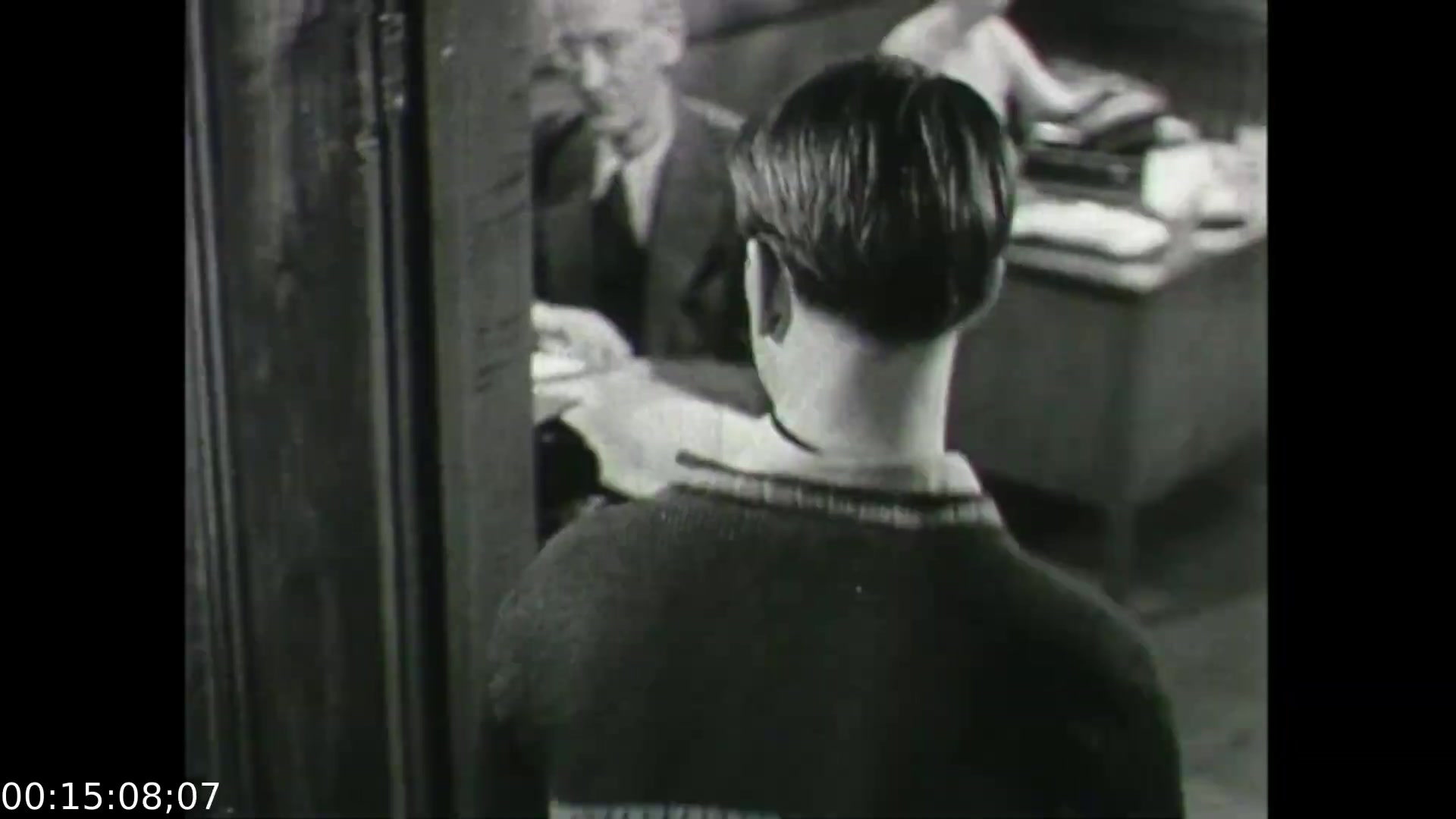 The still from 'Feelings of Depression' (1950) captures a pivotal moment in the film, showcasing John Murray in a contemplative state as he interacts with a doctor or counselor. The camera angle emphasizes his vulnerability, focusing on the back of his head while the professional figure is partially visible, suggesting an intimate yet formal setting. This visual choice enhances the theme of personal struggle with mental health, reflecting the film's educational aim of shedding light on depression in a post-war context, emphasizing understanding and empathy toward mental health challenges.