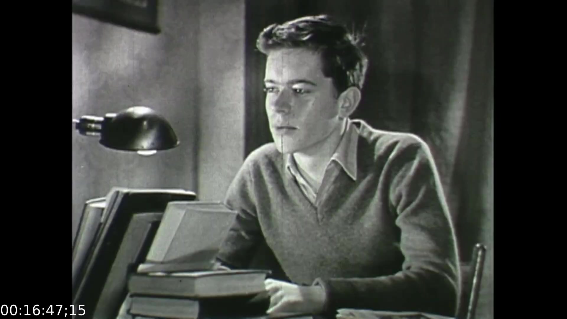 The still from 'Feelings of Depression' (1950) features a young man, presumably depicting John Murray, deep in thought at a desk cluttered with books. A desk lamp casts a focused light, accentuating his contemplative expression. The setting conveys a somber tone, reflecting themes of introspection and emotional struggle, central to the film's exploration of depression and mental health awareness during that era. The grayscale aesthetic emphasizes the seriousness of the subject matter.