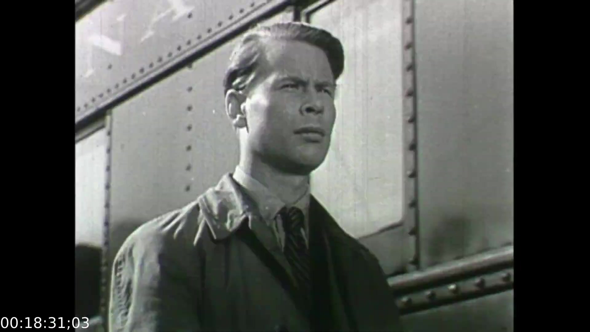 The still from 'Feelings of Depression' depicts a solemn male character, likely John Murray, standing in front of an industrial backdrop, suggesting a narrative centered on his internal struggle. The black-and-white aesthetic, typical of the era, enhances the film's serious tone, reflecting the themes of despondency and mental health. His expression conveys a sense of contemplation or concern, aligning with the film's exploration of emotional challenges faced by individuals in a post-war society. This educational dramatization aims to raise awareness about depression and promote understanding of mental health issues.