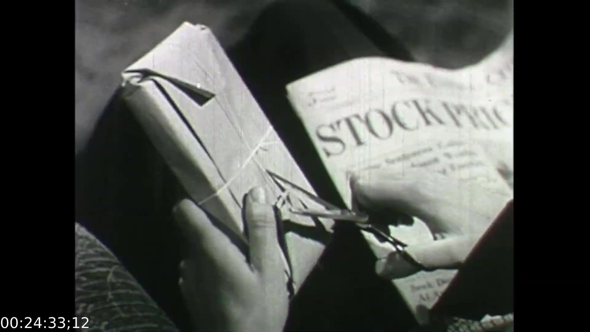 The still from 'Feelings of Depression' (1950) depicts a close-up of hands engaged in the act of cutting twine on a wrapped package. The hands are focused and deliberate, reflecting the attentiveness of the character, John Murray, a businessman facing emotional struggles. In the background, a newspaper headline that reads 'STOCK PRICE' hints at themes of business and financial pressures. This moment may symbolize his connection to work and the stress that contributes to his despondency. The black-and-white imagery enhances the film's historical context and emotional tone.