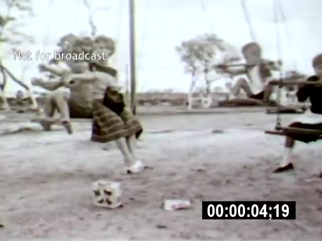 The 16mm film still from 'Brasilia' captures children playing on swings in a park setting, emphasizing a sense of joy and innocence. The low camera angle enhances the perspective of the children, with the surrounding trees and empty space contributing to a feeling of openness in the new urban landscape.