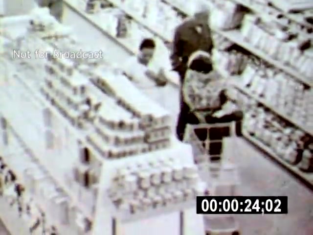 The still from 'Brazilia' captures a busy supermarket scene, where shoppers navigate aisles filled with various products. The overhead camera angle provides a unique perspective, highlighting the interactions among the individuals, including a woman with a shopping cart and others discussing nearby.