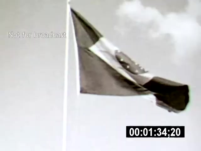 The still features a Brazilian flag waving prominently against a cloudy sky, captured from a low angle that emphasizes the flag's height and movement. The monochrome tones contribute to a nostalgic or historical feel, harking back to Brazil's cultural identity and national pride.