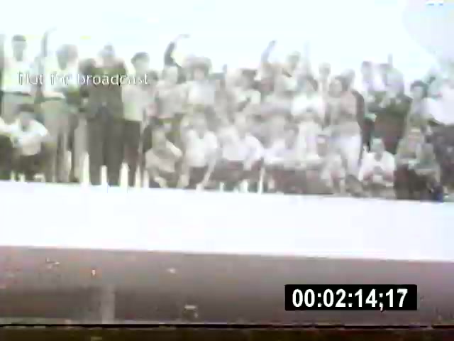 The film still captures a large group of people, likely celebrating or gathering, with a view from above that emphasizes their collective presence. The setting appears to be an urban environment in Brasília, showcasing the vibrant community spirit of the city.