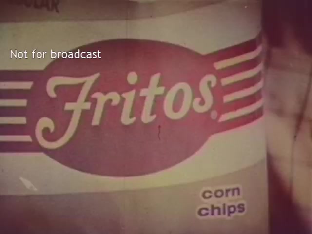 The still features a close-up view of a Fritos bag, prominently displaying the brand name in bold, flowing letters against a colorful background. Below the brand name, the text 'corn chips' is included, indicating the product type. The image is likely colorized, providing a retro aesthetic reminiscent of 16mm film, with a watermark stating 'Not for broadcast.'